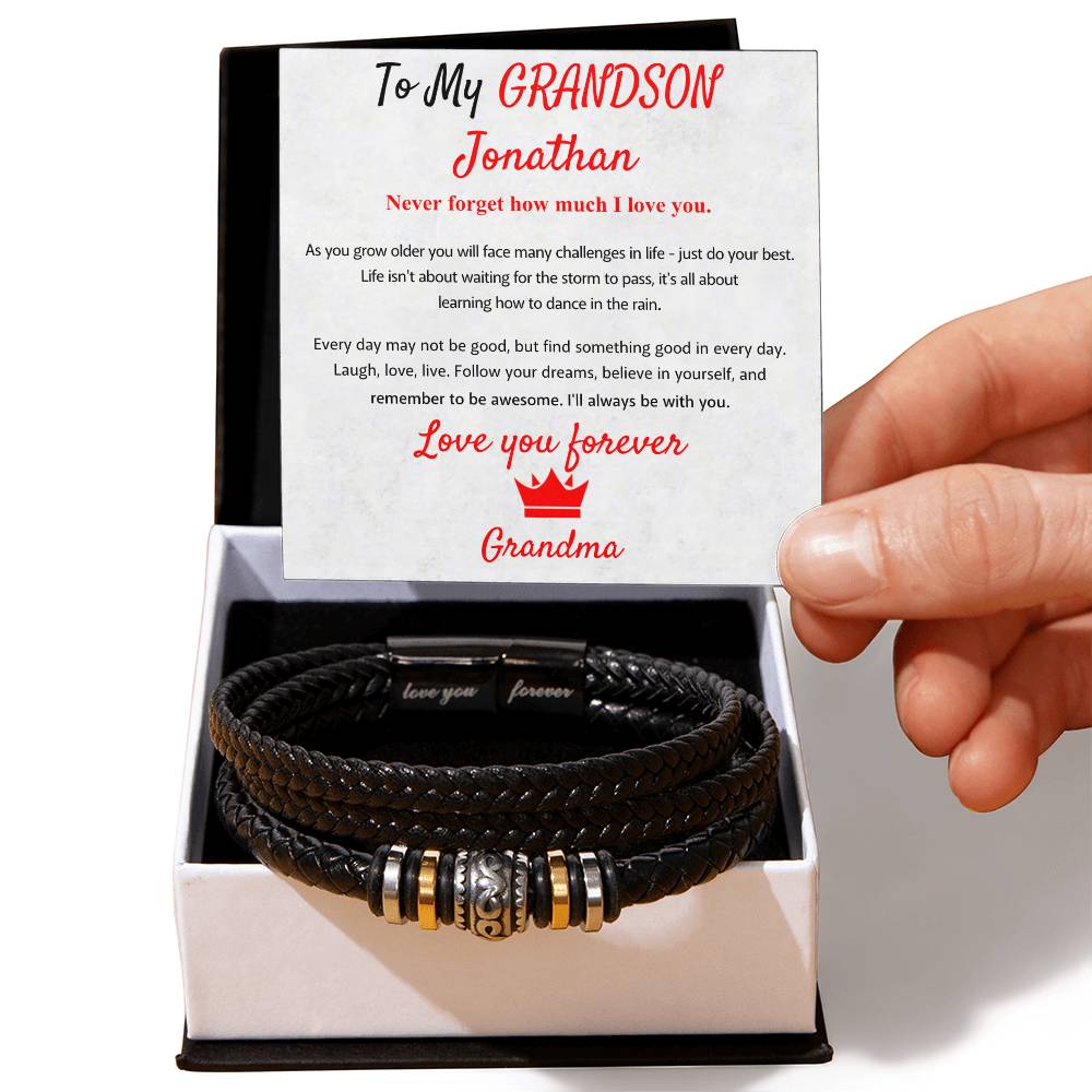 Black leather bracelet with charms in a box, held by a hand, with a personalized message card from 'Grandma'.